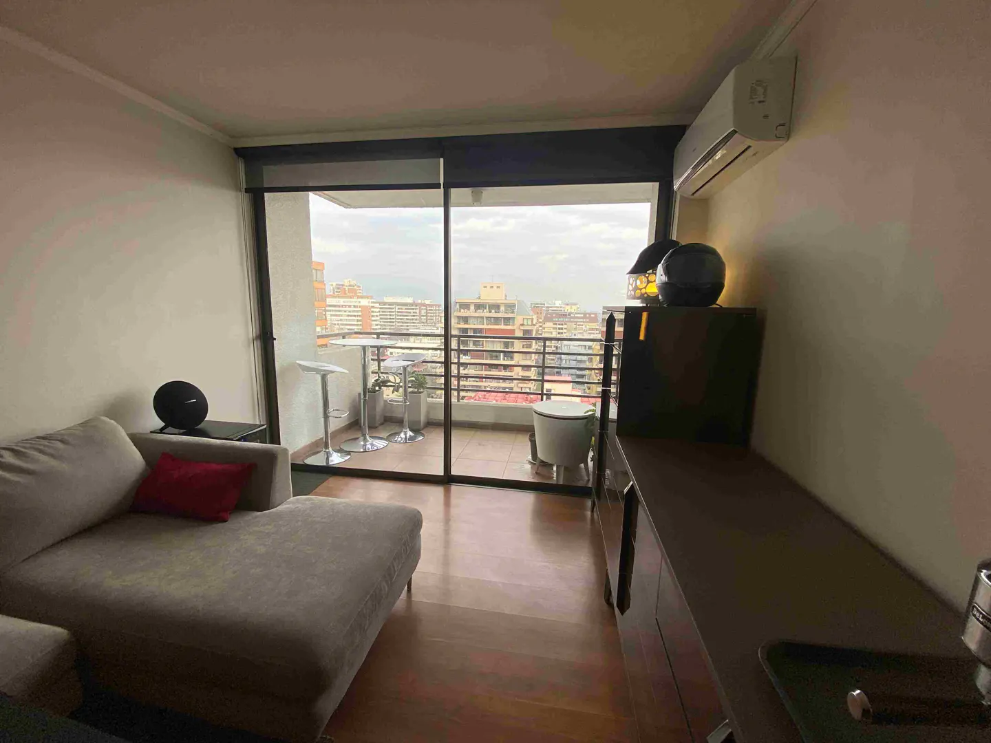 Living room with a gray chaise lounge, red pillow, and a balcony with a city view.