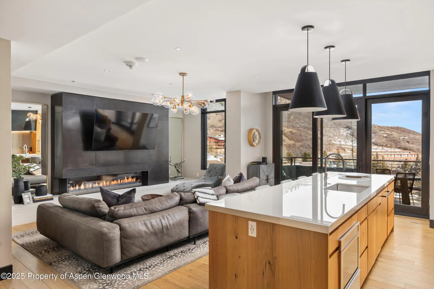 Modern open-concept living room with a grey sectional, fireplace, and kitchen island with three black pendant lights.