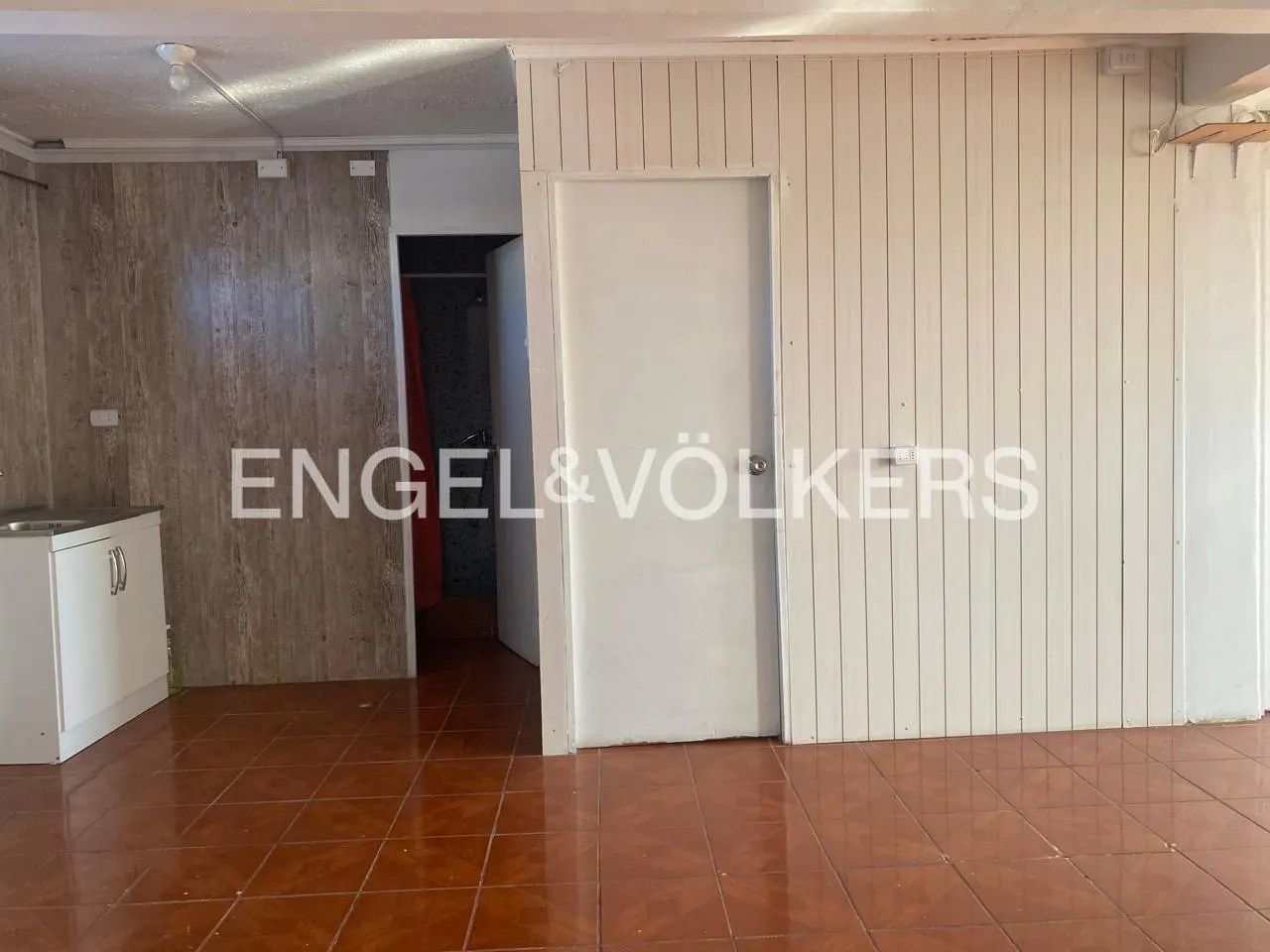 An interior shot of a room with brown tile floors, white cabinets, and white wood-paneled walls. A doorway leads to another room.