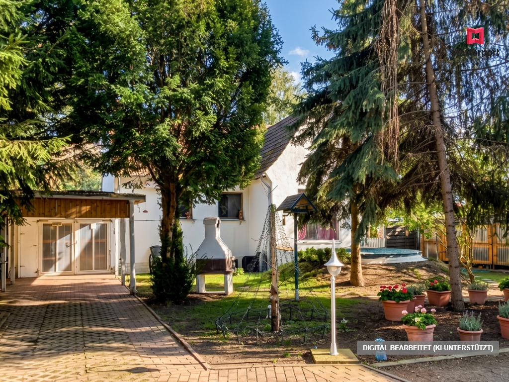 A white house with a paved driveway, outdoor fireplace, and a garden with potted flowers and tall evergreen trees. [AI-generated text]