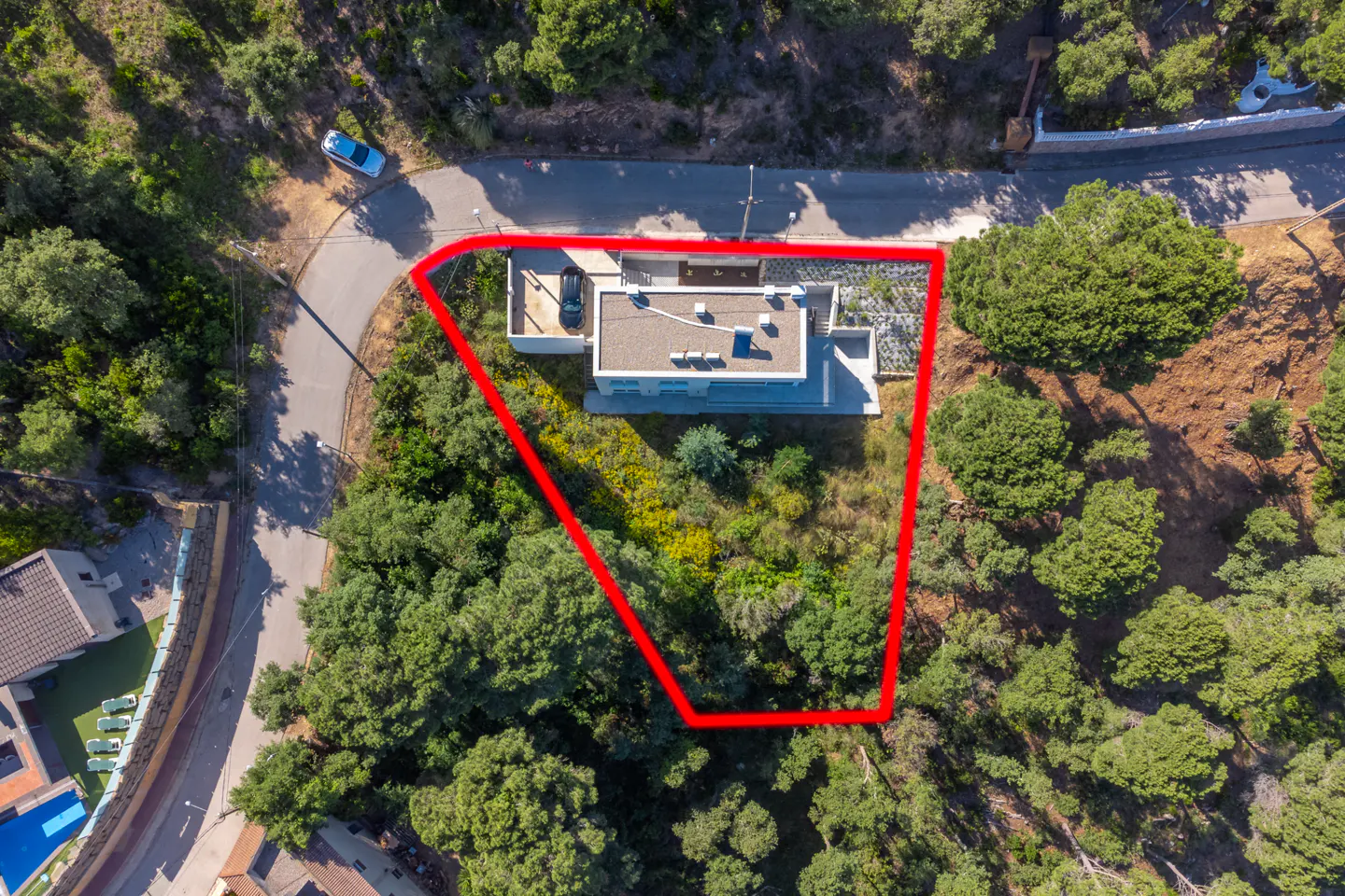 Aerial view of a modern house surrounded by trees, with a red outline highlighting the property boundary.