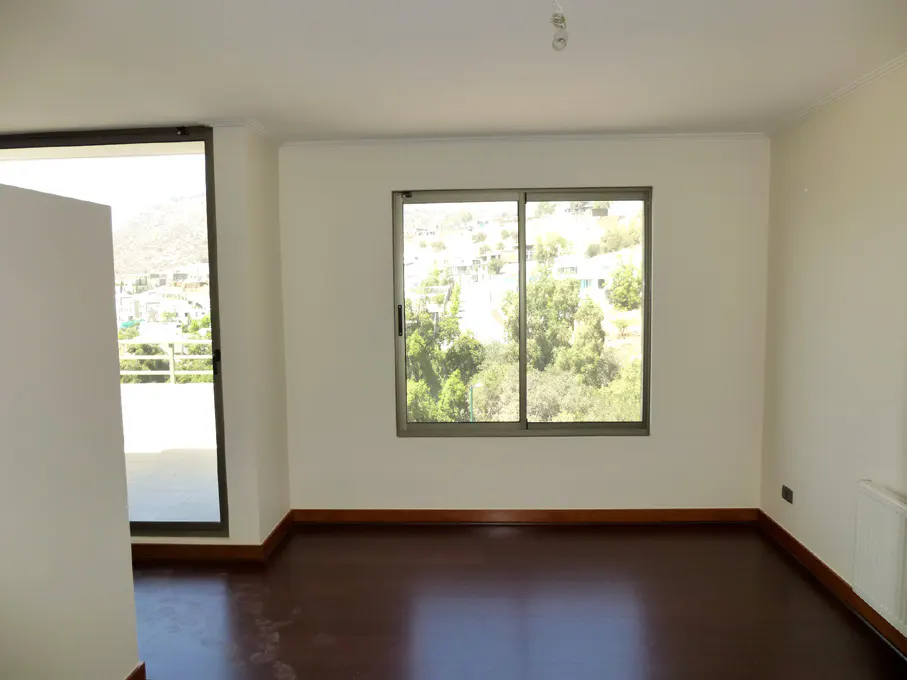 Bright, empty room with dark wood floors, white walls, and a sliding glass window overlooking a green, hilly landscape.