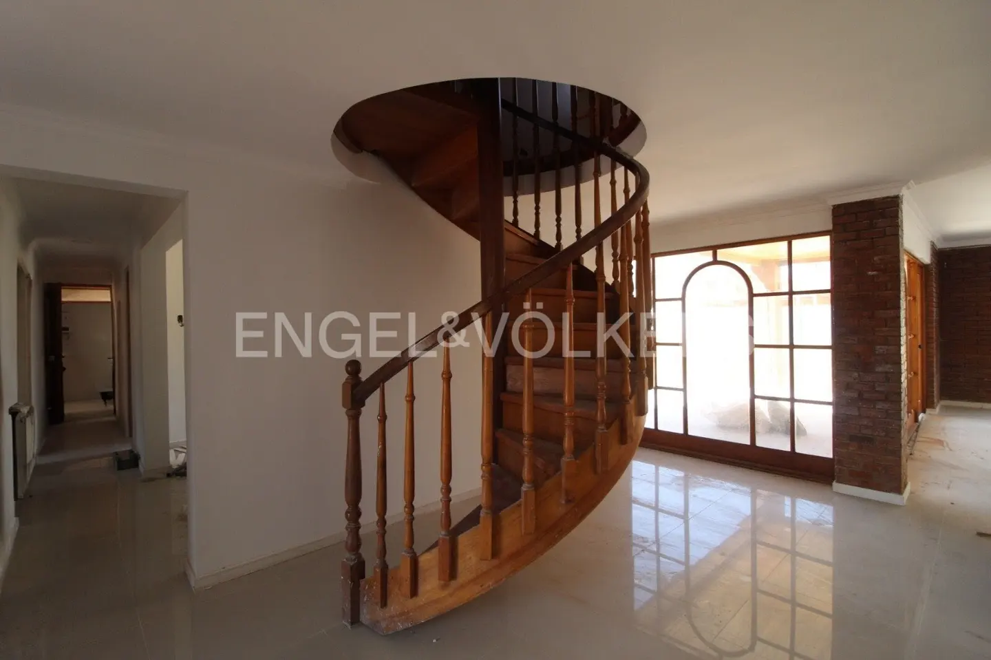 A bright room with a wooden spiral staircase, large windows, and a hallway.