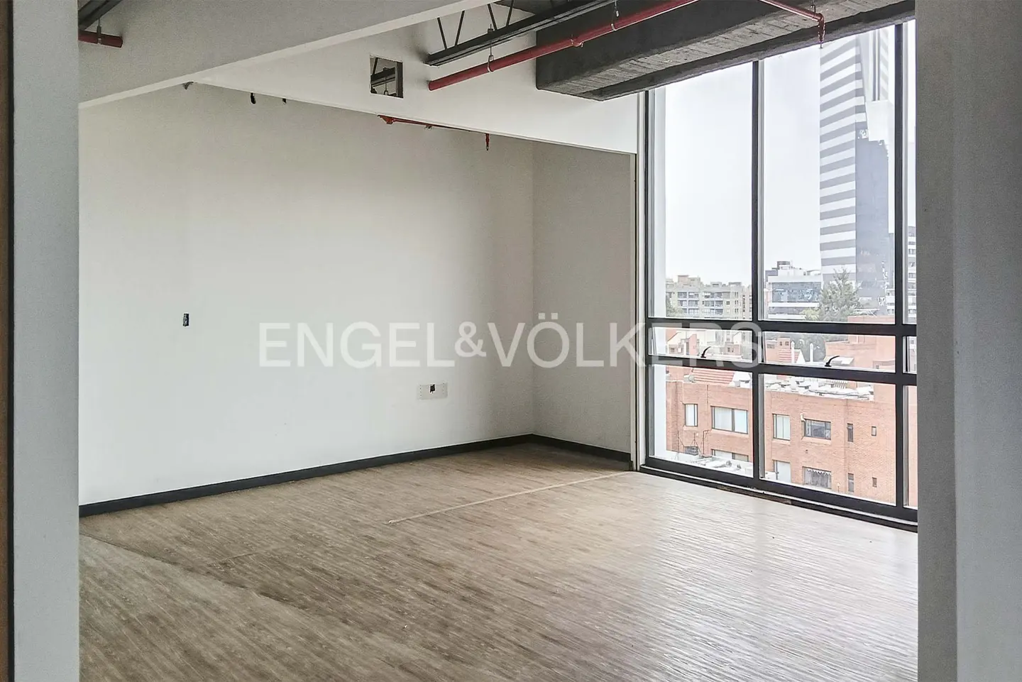 An empty room with wood floors, white walls, and a large window showing a city view.