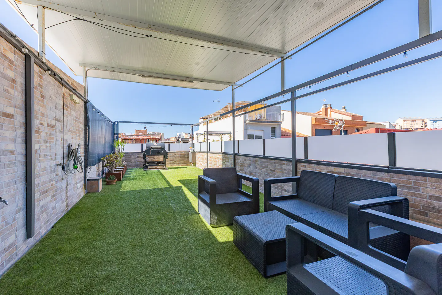 Outdoor rooftop patio with artificial grass, black wicker furniture, brick walls, and a grill in the background.
