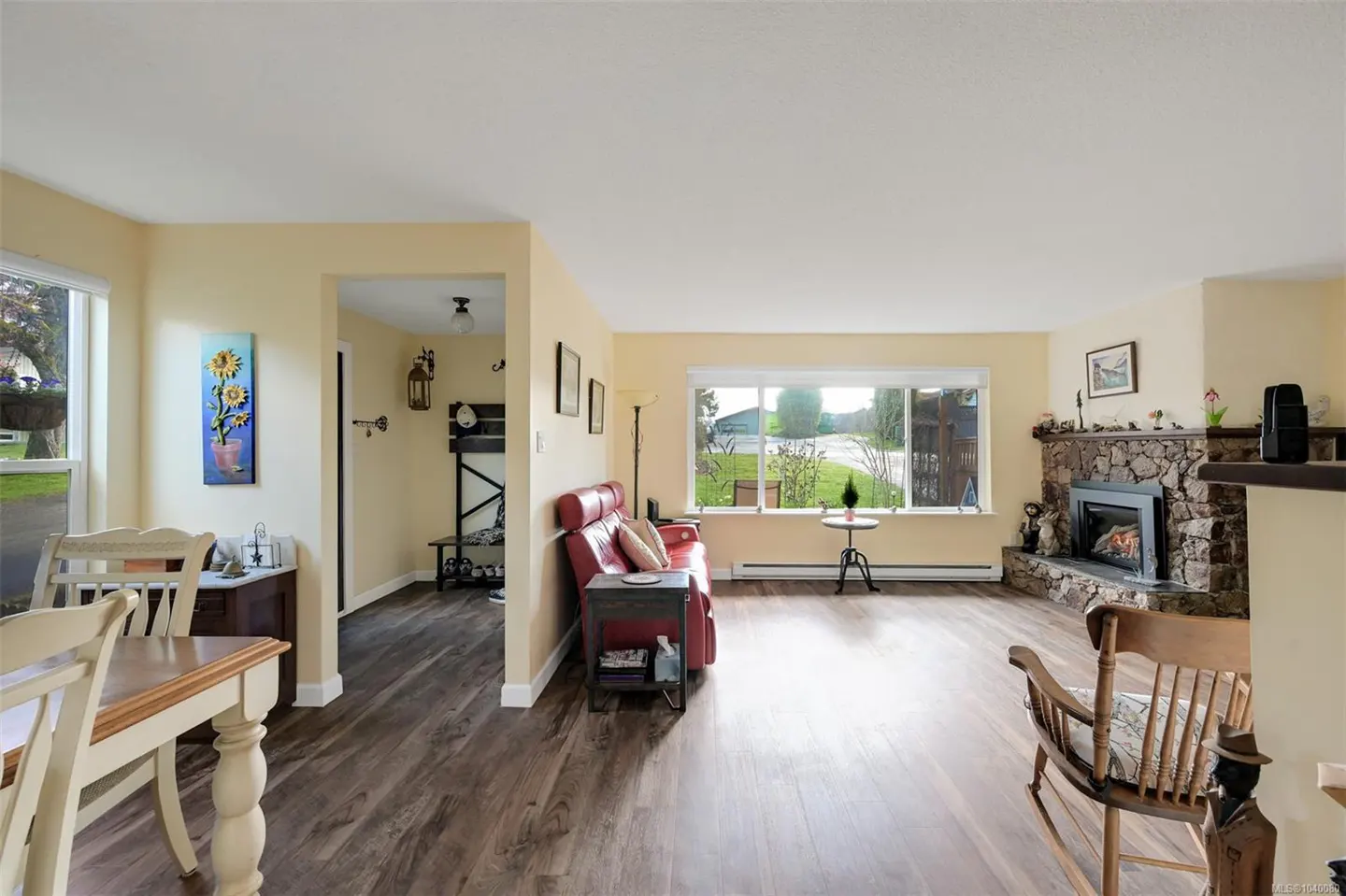 Bright living room with wood floors, a red sofa, a stone fireplace, and a dining area with a sunflower wall art piece.