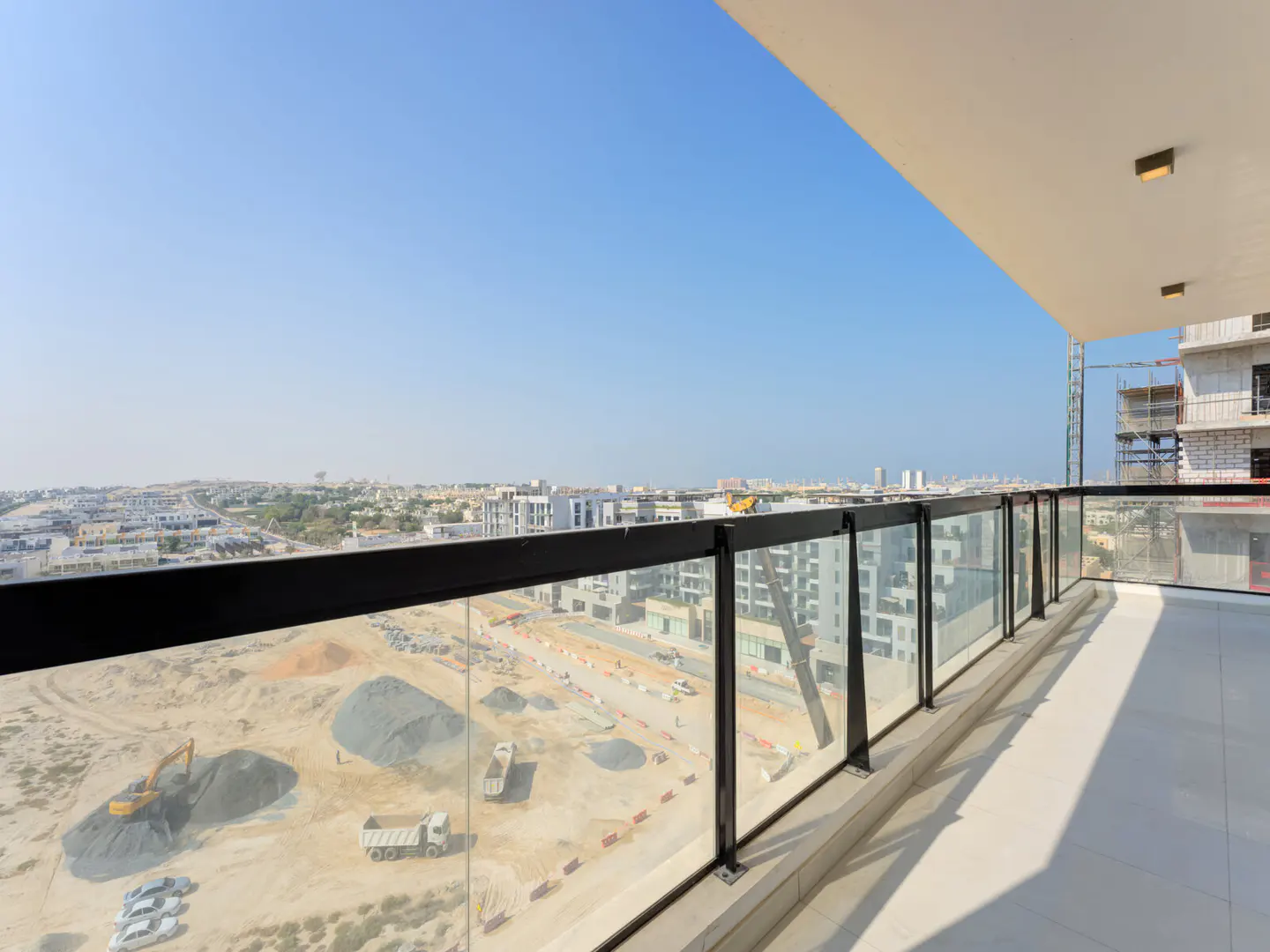 Balcony view of a construction site with heavy machinery and piles of dirt under a clear blue sky.