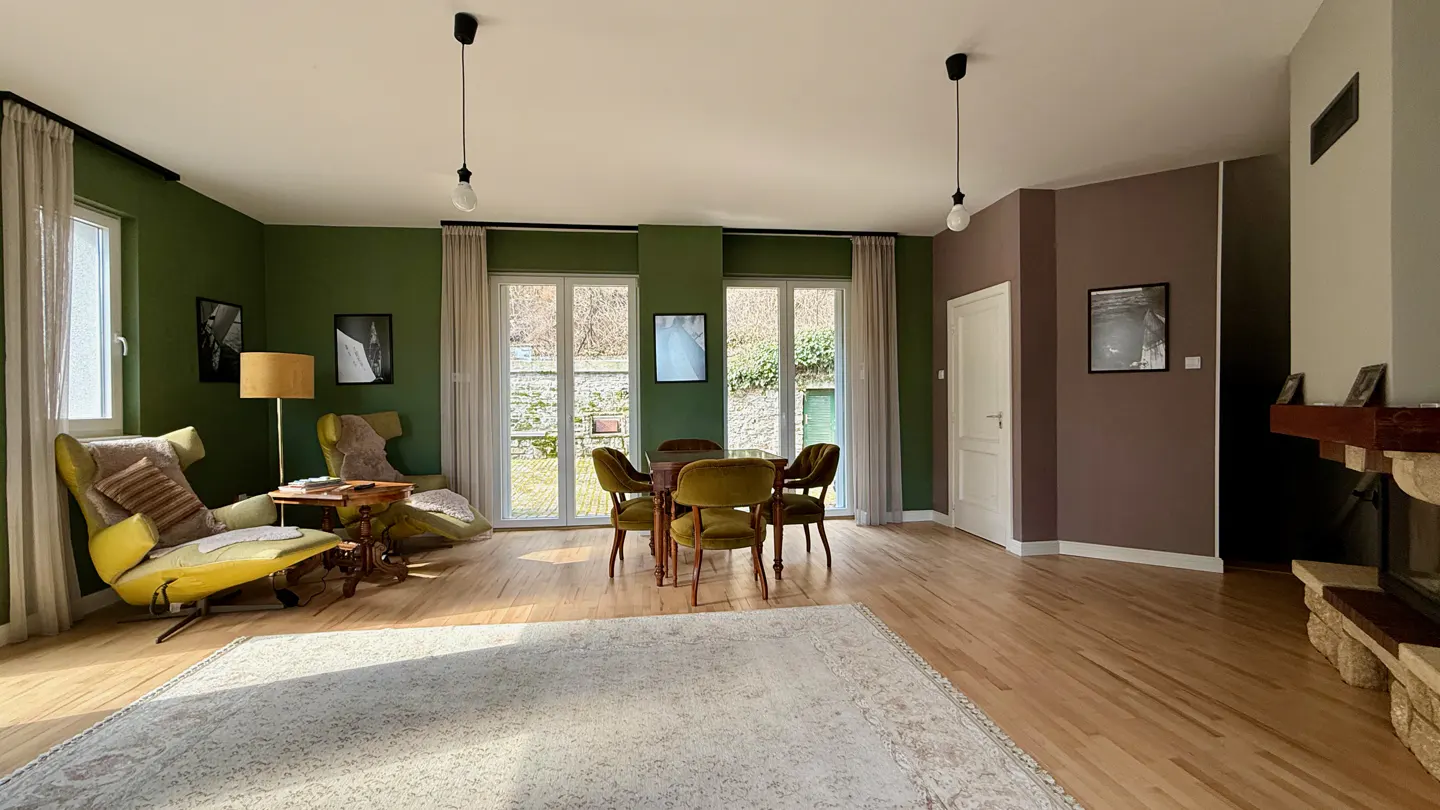 A living room with green and brown walls, wood floors, a dining table with green chairs, and a yellow armchair.