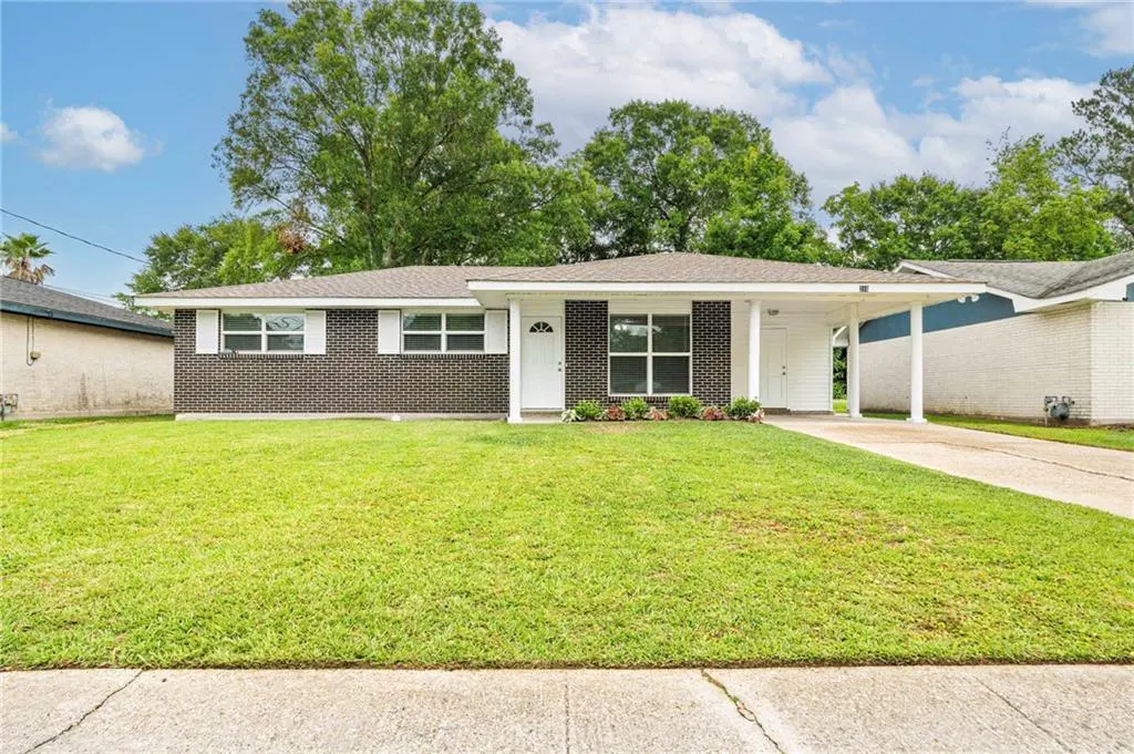 A single-story brick house with a green lawn and a white carport.