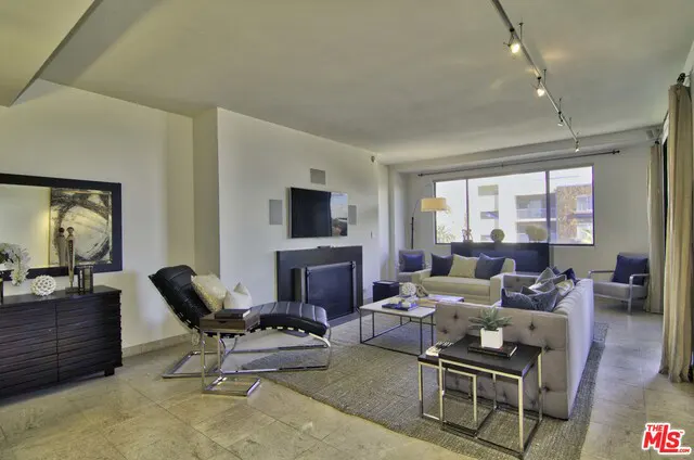 Bright living room with a black fireplace, TV, and a black leather chaise lounge. Sofas and chairs are arranged around a coffee table.
