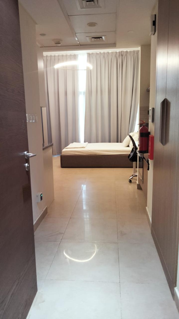 A view from a doorway into a modern bedroom with a low bed, white curtains, and a desk chair on a glossy tiled floor.