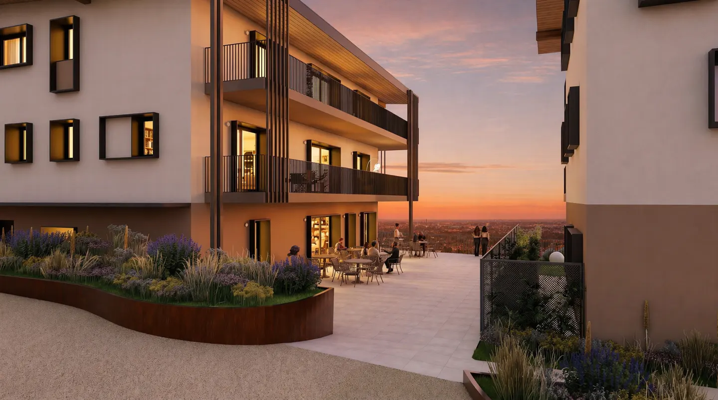 Exterior view of a modern apartment building with balconies, a patio with tables and chairs, and a sunset in the background.
