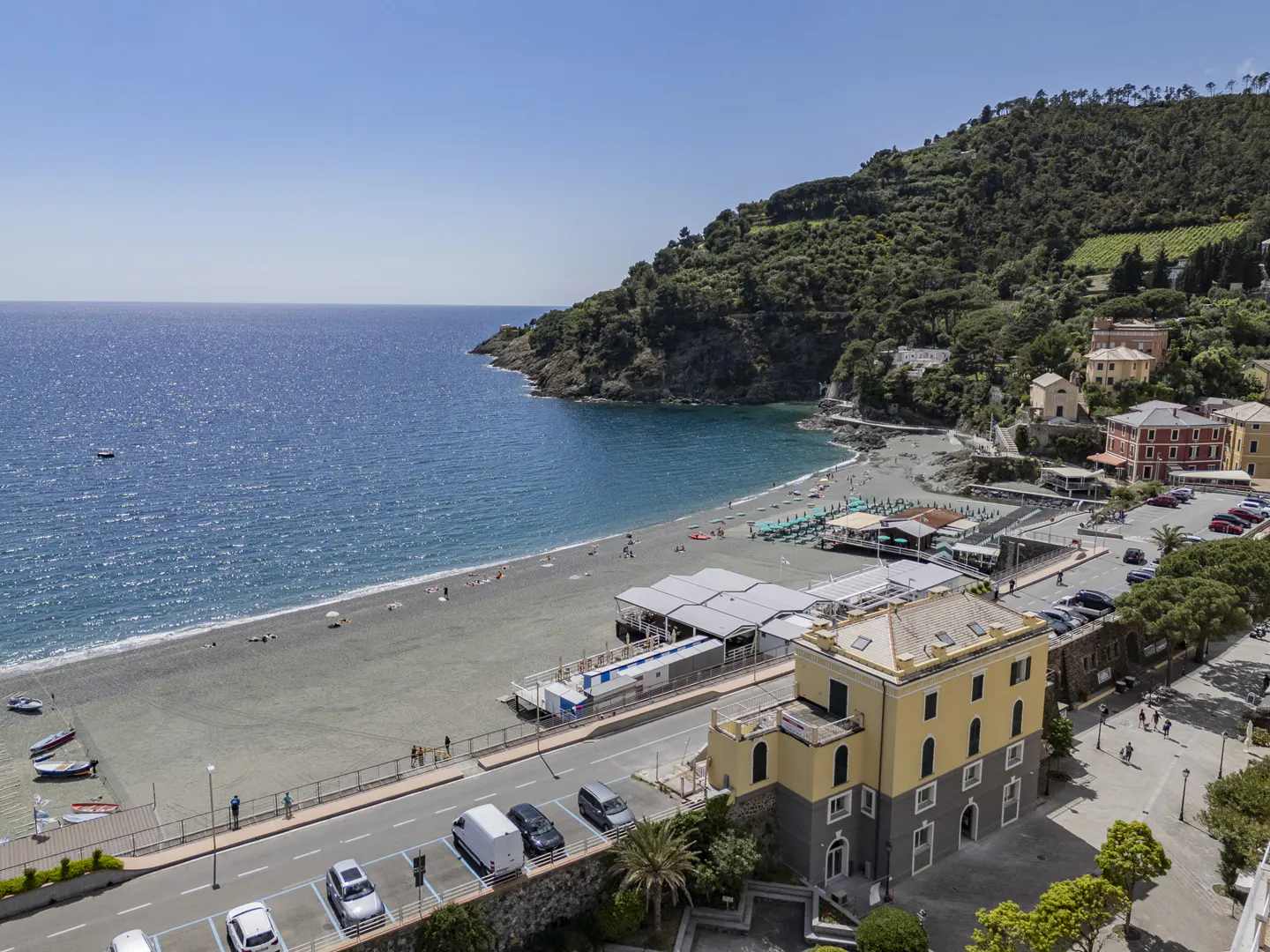 Aerial view of Moneglia, Italy, featuring a beach, blue sea, and buildings against a green hillside.