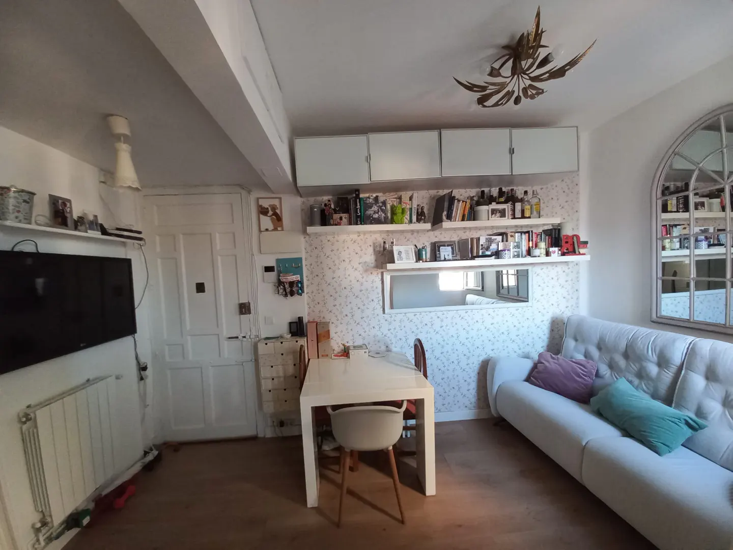 A living room with a white sofa, a white table with chairs, and shelves with books and decorations.