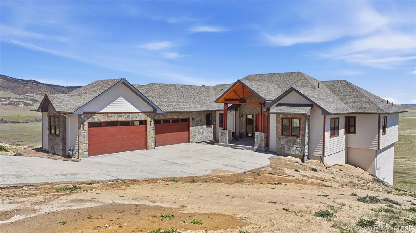 Exterior view of a two-story house with stone and siding, a gray roof, and a red garage door.