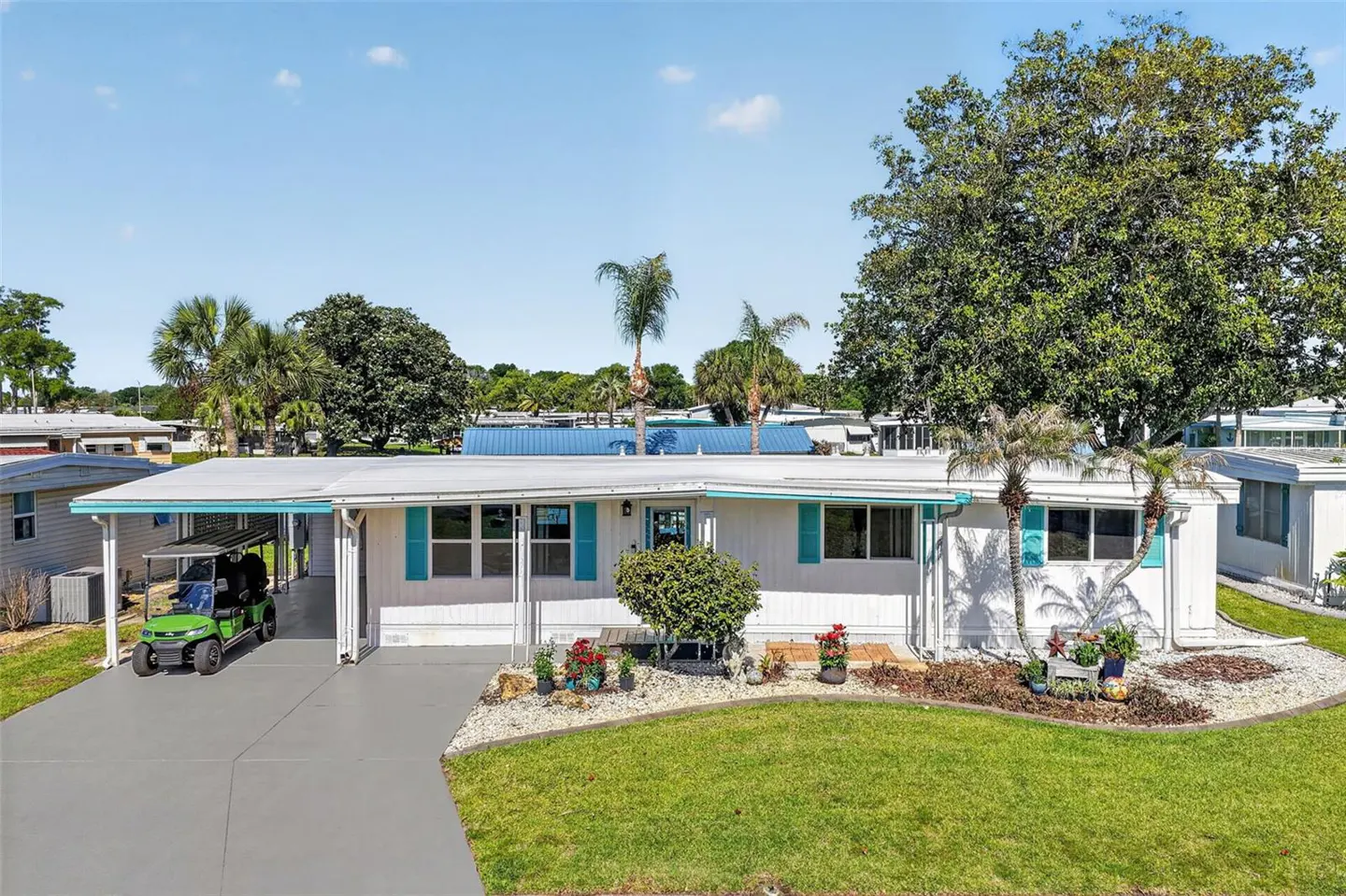 Exterior of a white mobile home with turquoise shutters, a green golf cart, and a well-manicured lawn.