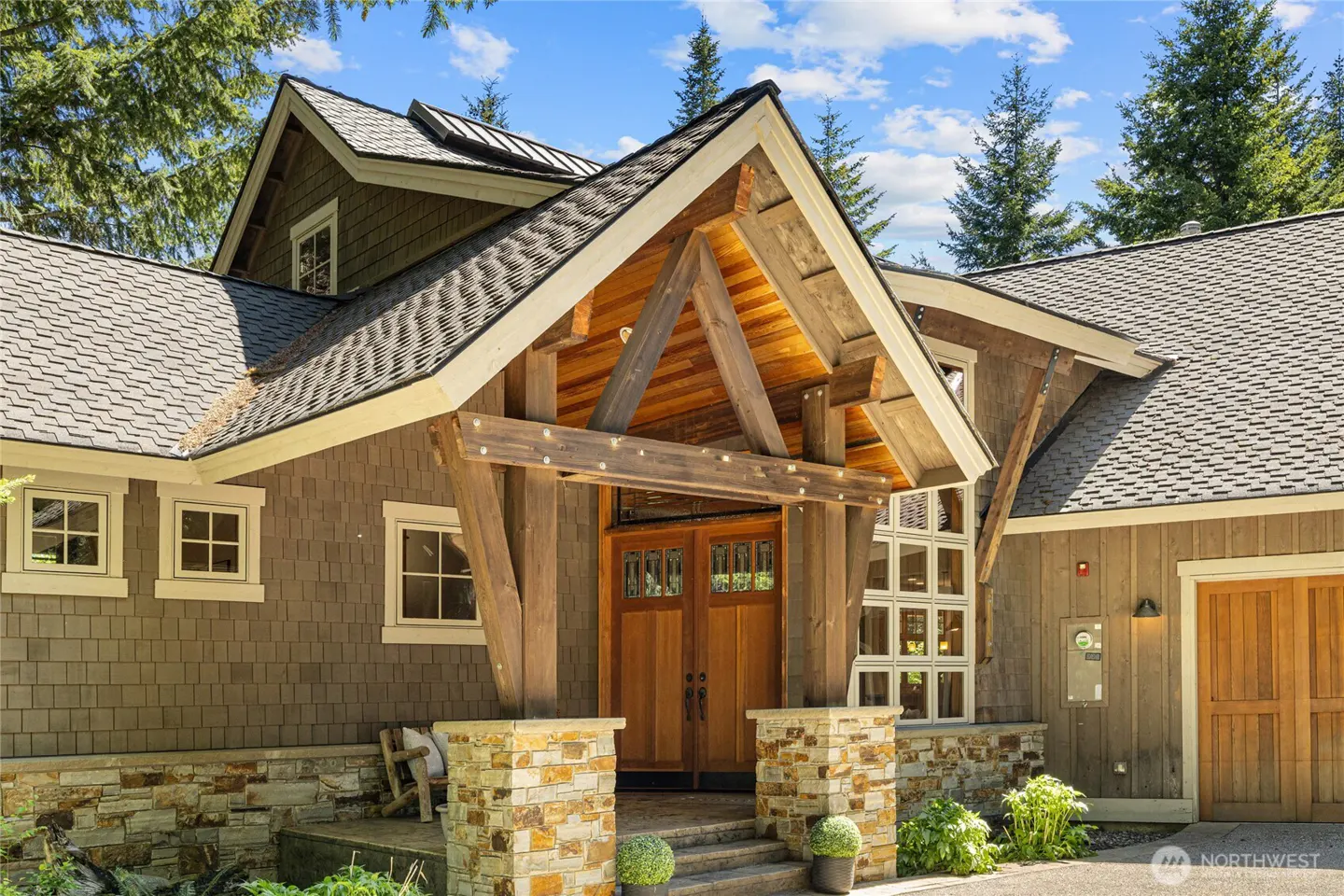 Exterior of a craftsman-style home with a timber-framed entryway, stone base, wood siding, and double wooden front doors.