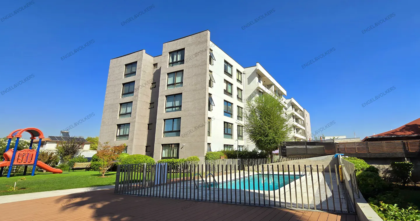 Exterior view of a modern apartment building with a pool, playground, and green lawn under a clear blue sky.