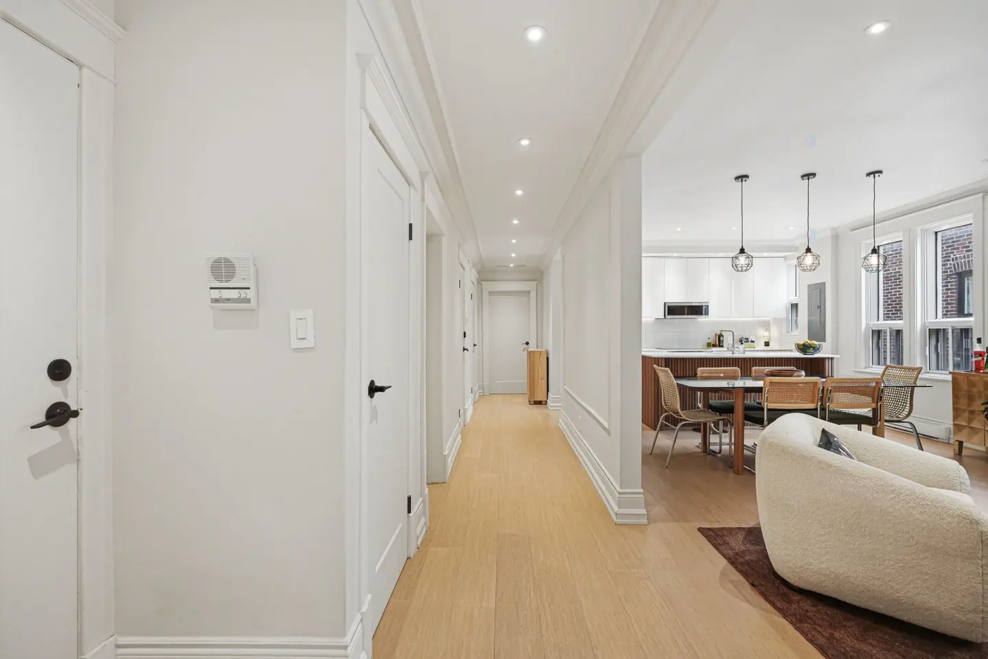 Bright hallway with white walls, doors, and trim, leading to an open-concept kitchen and living area with wood floors and modern furnishings.