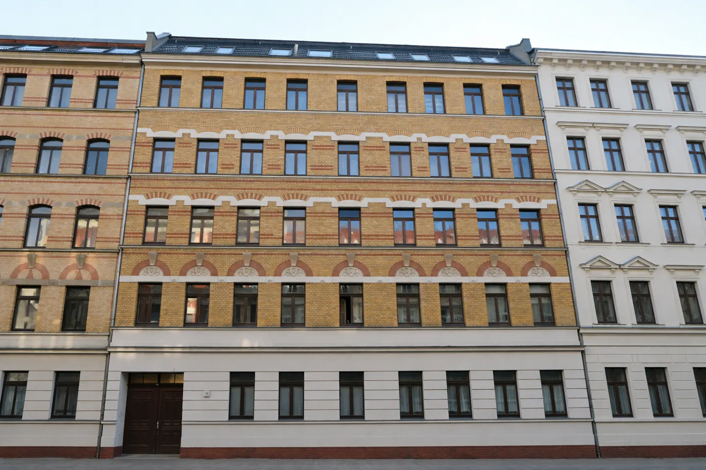 Three adjacent apartment buildings, each with multiple stories and many windows, in yellow, tan, and white.
