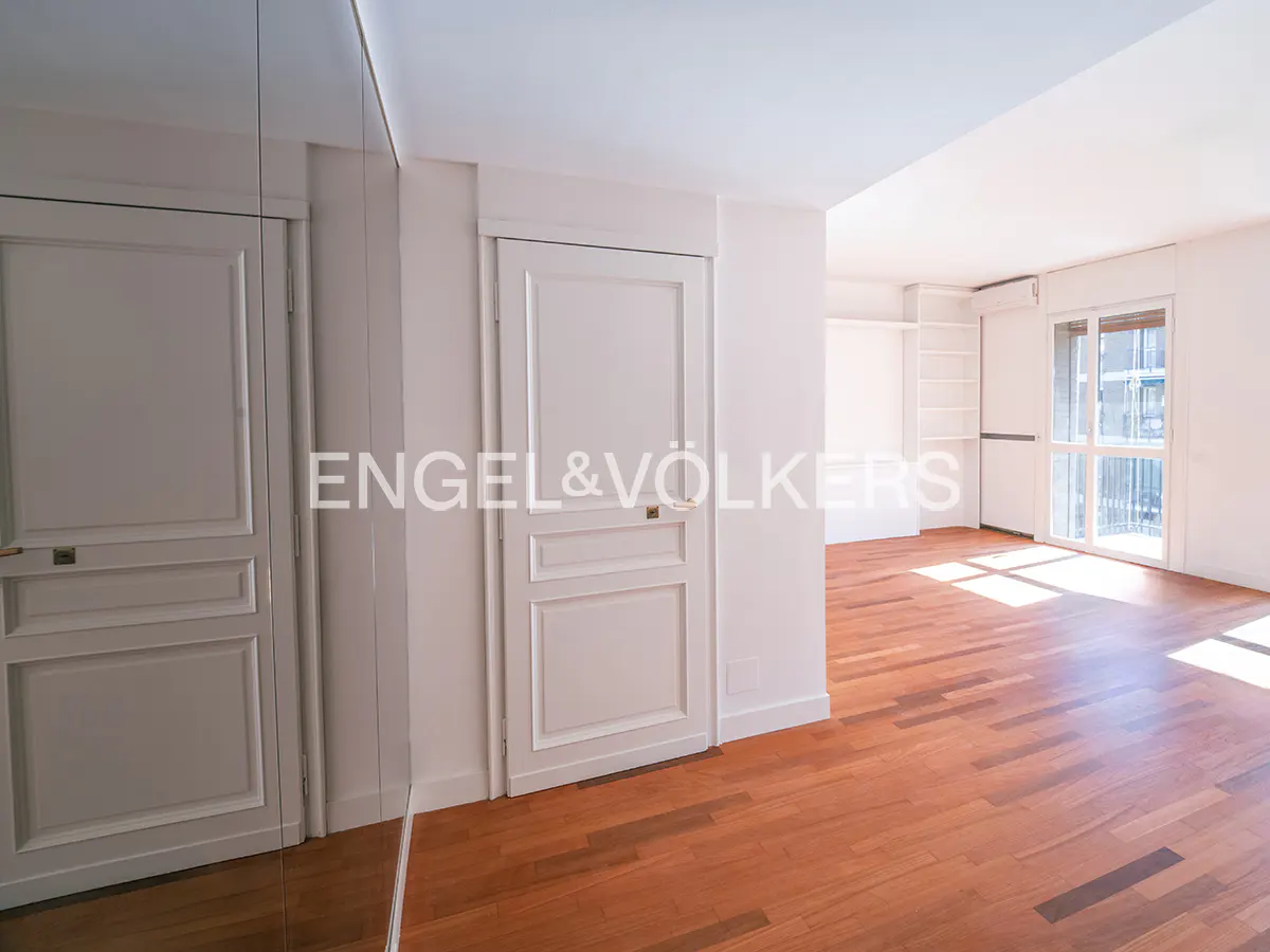 Bright room with white paneled doors, hardwood floors, built-in shelving, and a glass door leading to a balcony.