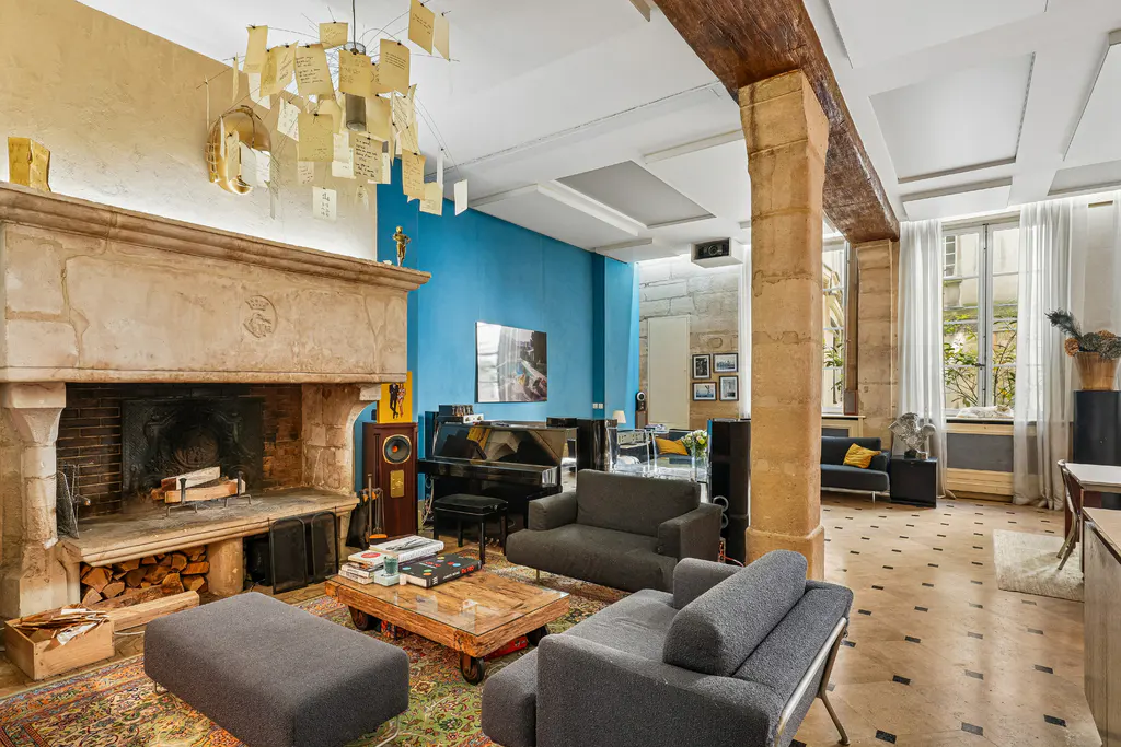 Living room with stone fireplace, blue accent wall, and grand piano. Gray sofas and a unique chandelier add character.