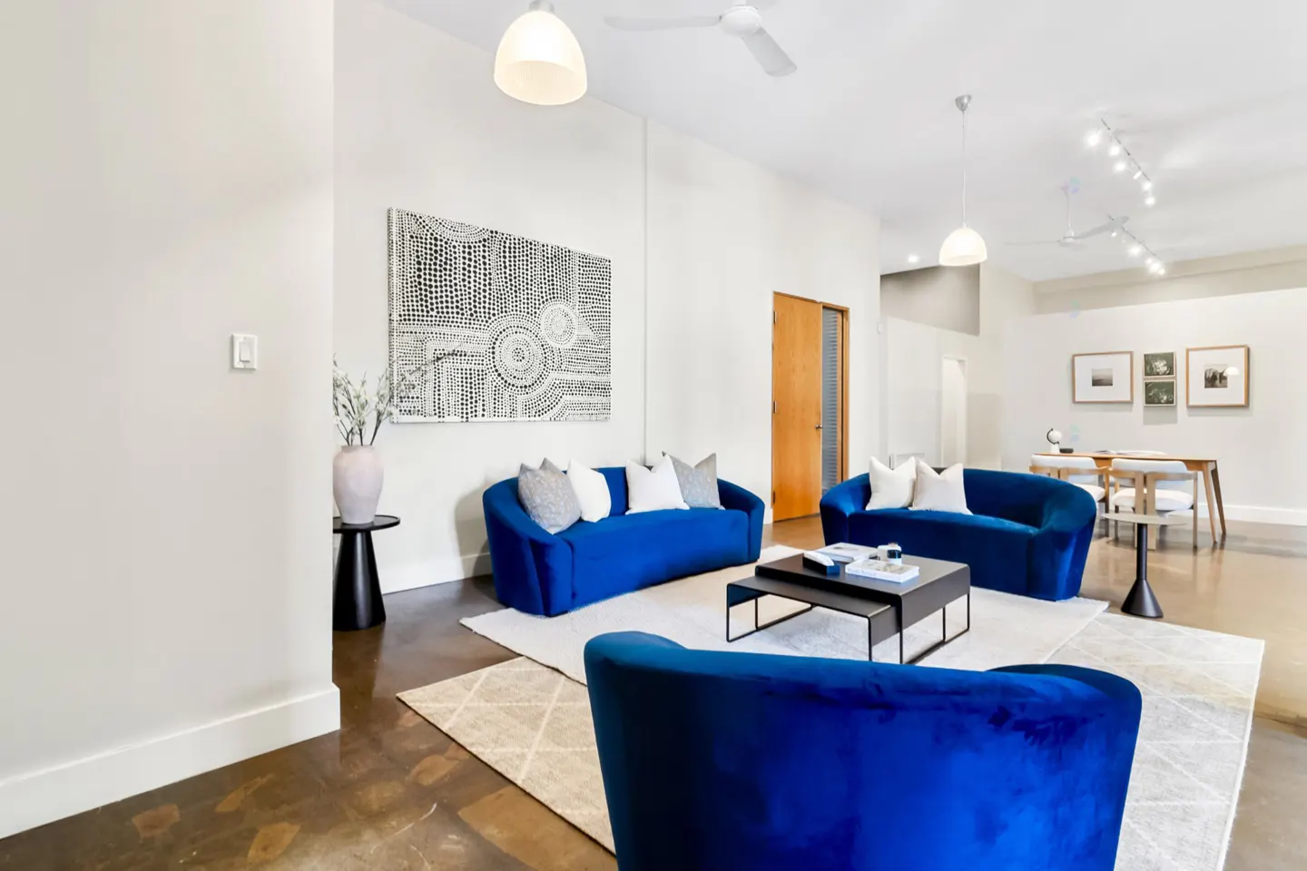 Bright living room with three blue sofas, a black coffee table, and a large black and white painting on the wall.