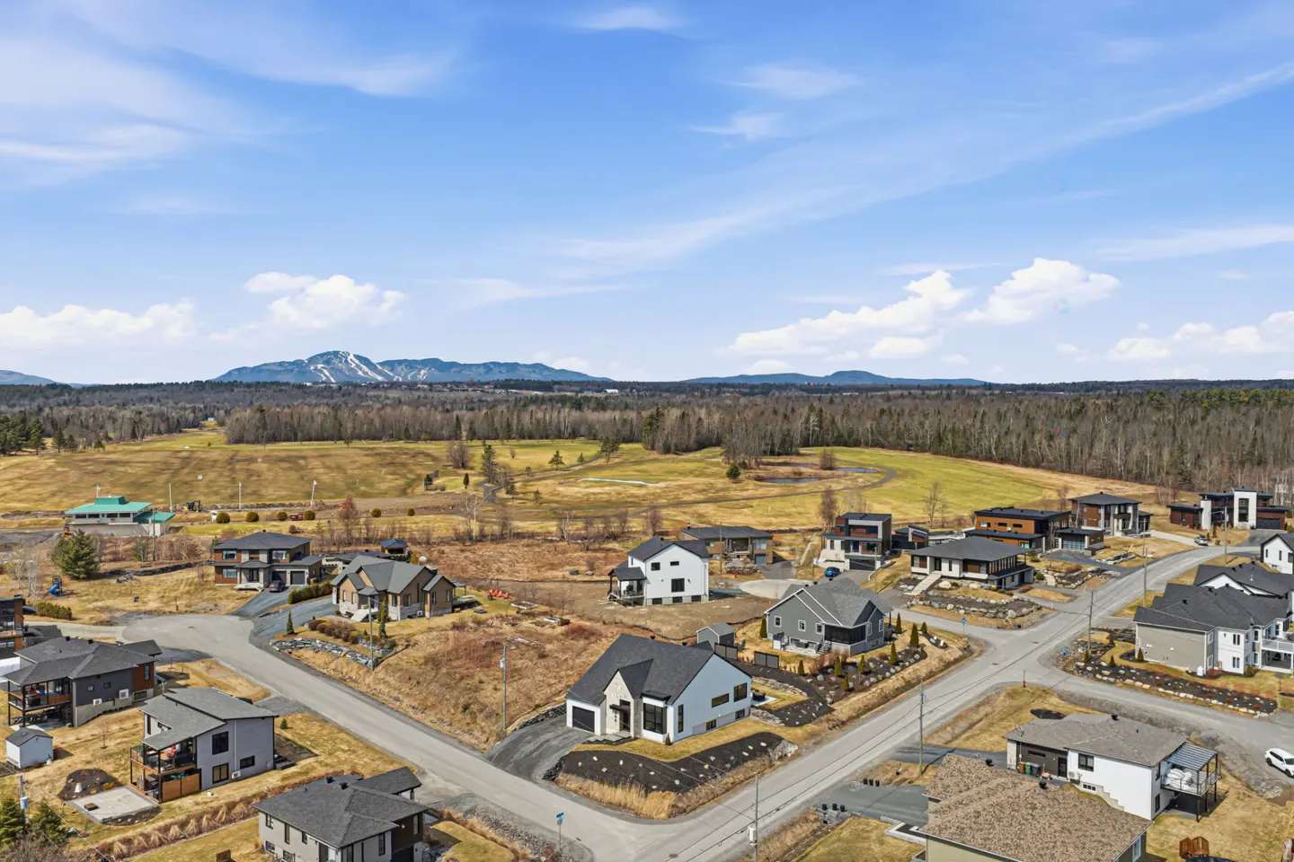 Aerial view of modern homes in a neighborhood with a golf course and mountains in the background under a blue sky.