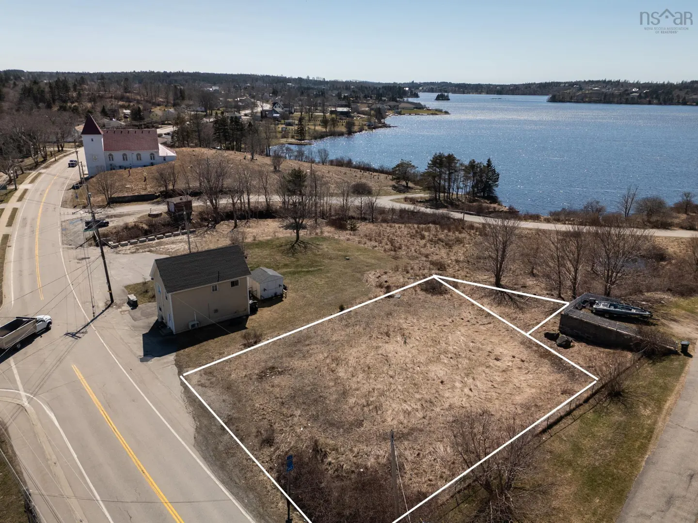 Aerial view of a vacant lot outlined in white, near a road, a church, and a body of water.