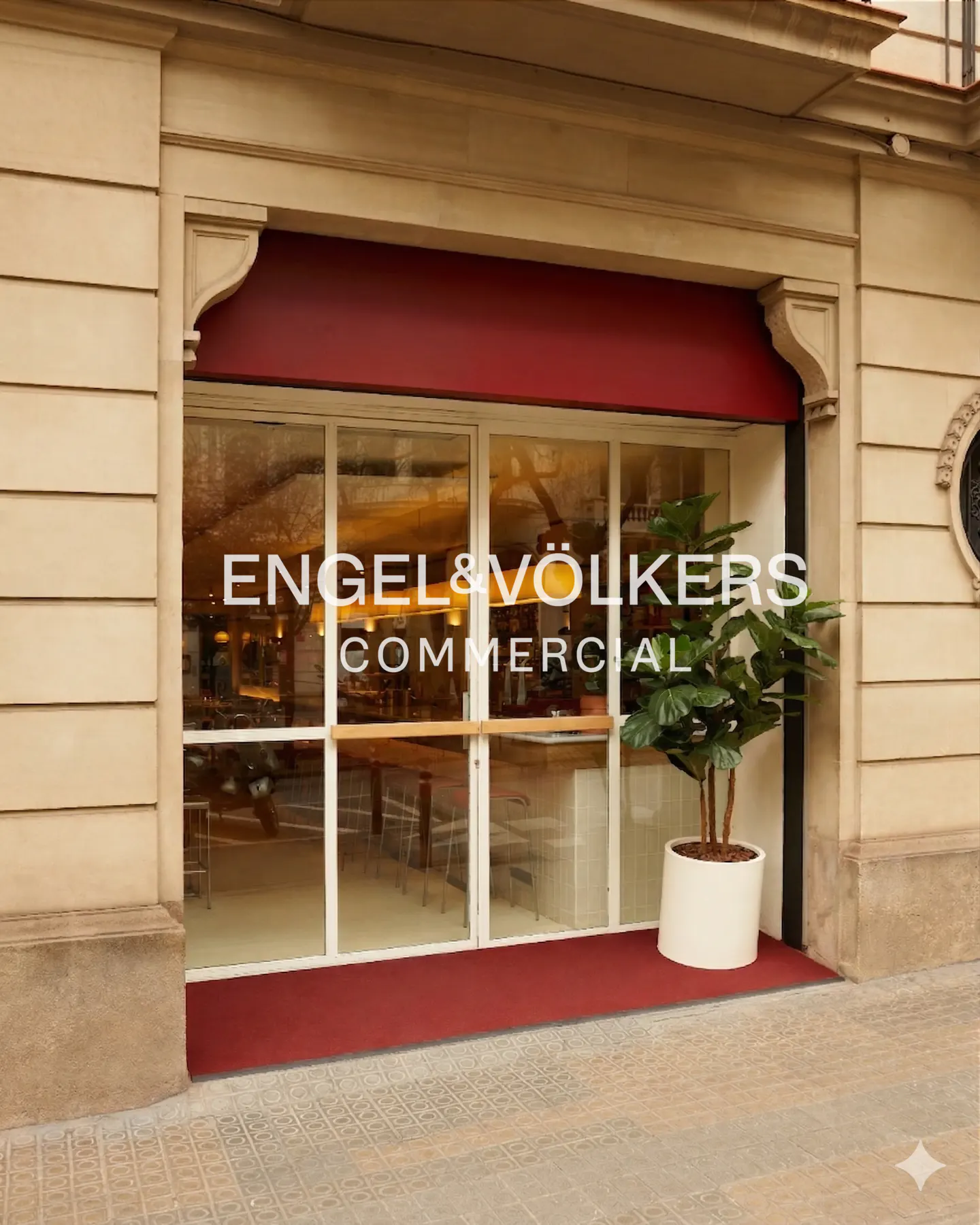 Engel & Völkers Commercial storefront with a red awning and mat. A potted plant sits to the right of the glass doors.
