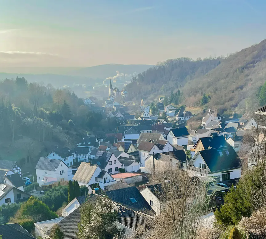 Scenic view of a village nestled in a valley, featuring houses, trees, and a church steeple in the distance.