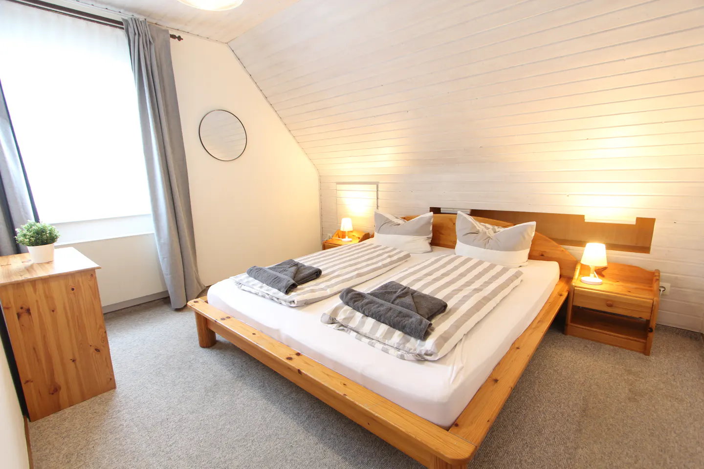 Bedroom with a wooden bed frame, white and gray striped bedding, gray towels, and wooden nightstands with lamps.