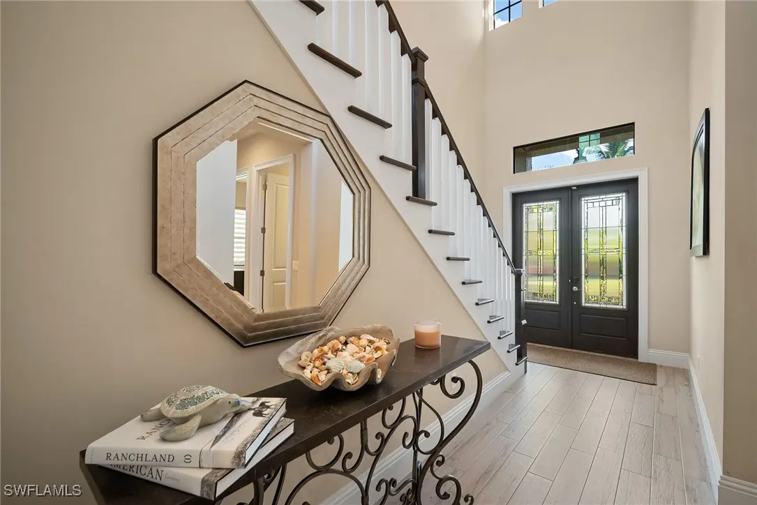 Foyer view with staircase, front door, and console table. Octagon mirror hangs above table with books, turtle figurine, and seashell bowl.