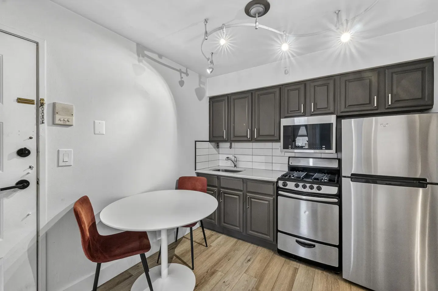 Small kitchen with dark grey cabinets, stainless steel appliances, white subway tile backsplash, and a round dining table.