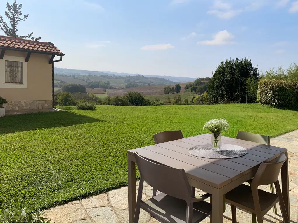 Outdoor patio with a table, chairs, and a vase of flowers overlooking a green lawn and rolling hills.