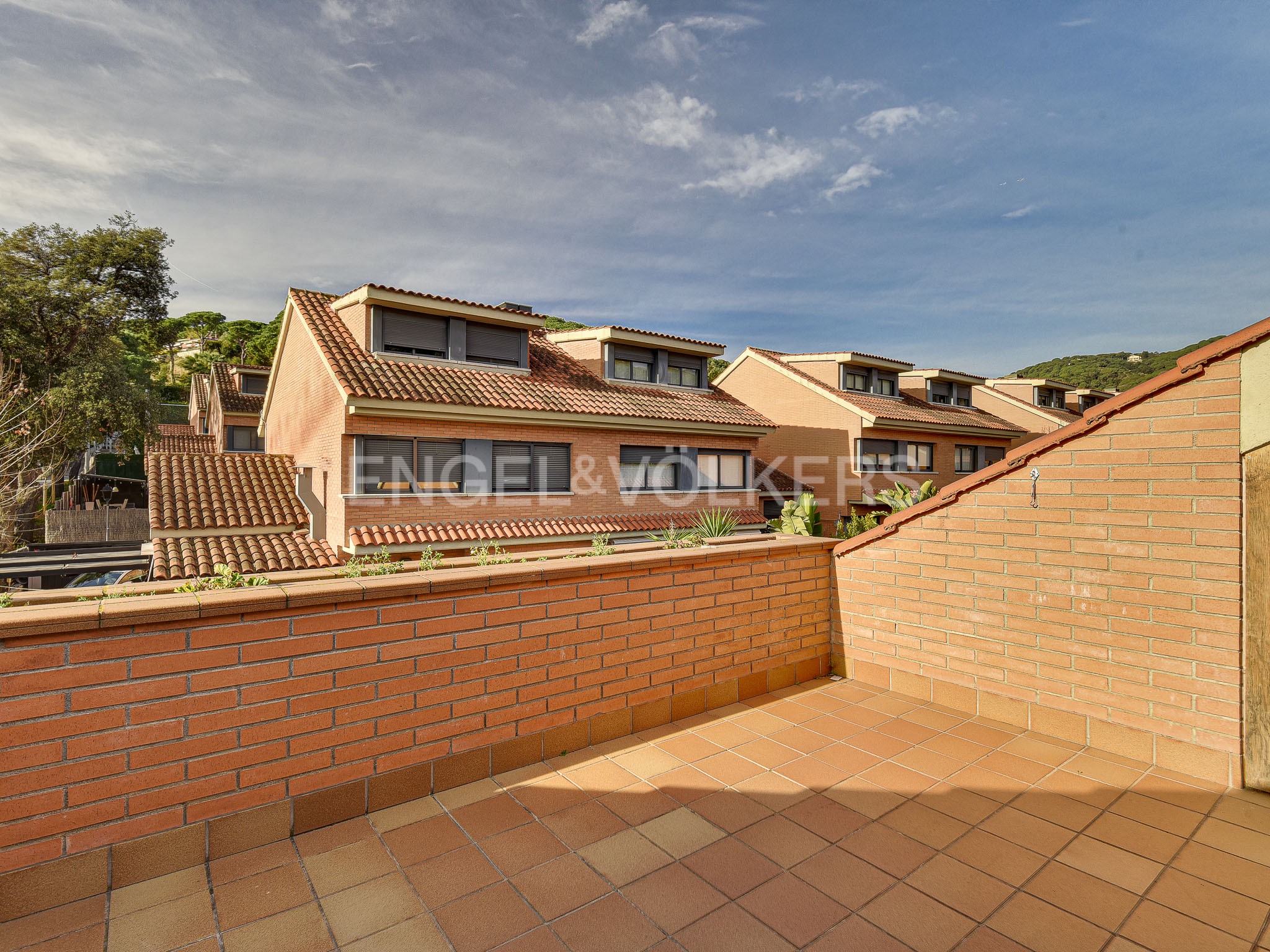 View from a terracotta-tiled balcony of a row of peach-colored townhouses with red-tiled roofs under a cloudy sky.