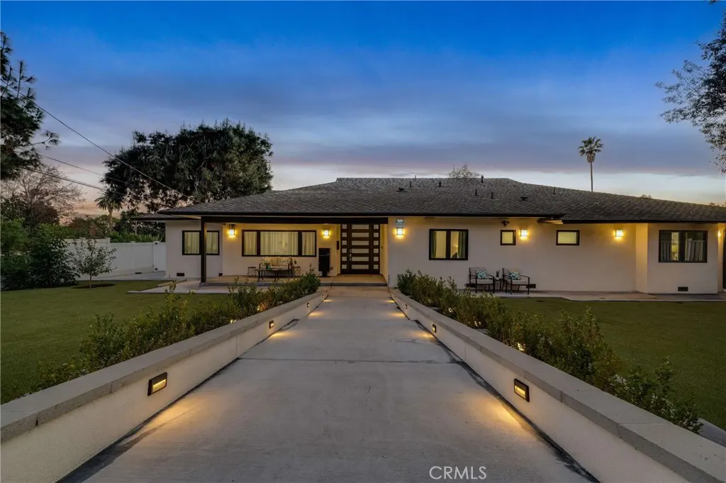 Exterior shot of a one-story white house with a dark roof and black trim, a concrete walkway, and green lawn at dusk.
