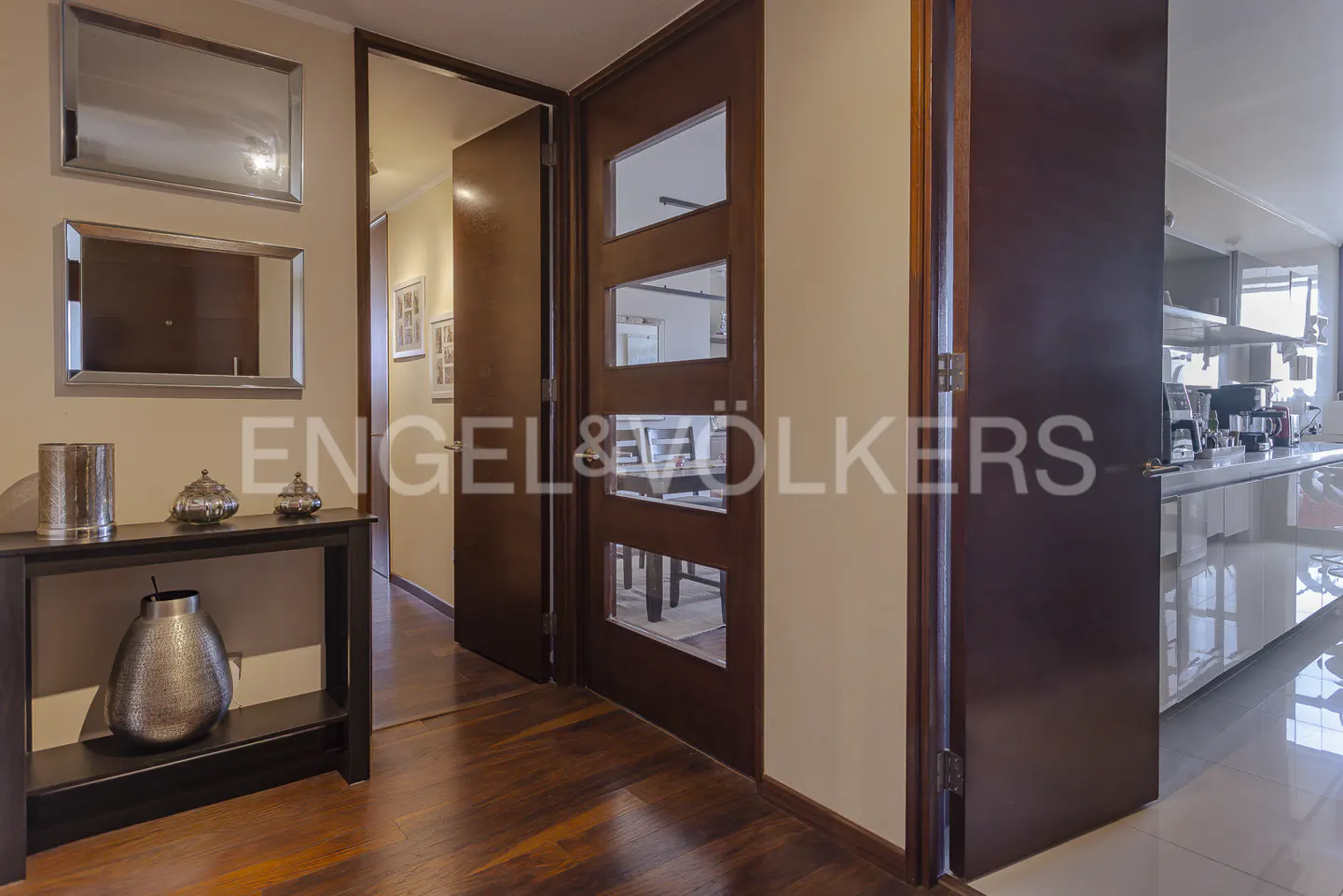 Hallway with dark wood floors, a console table with silver decor, and a door with glass panels leading to a dining room.