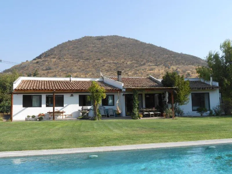 A white house with a red tile roof overlooks a green lawn and blue pool, with a hill in the background.