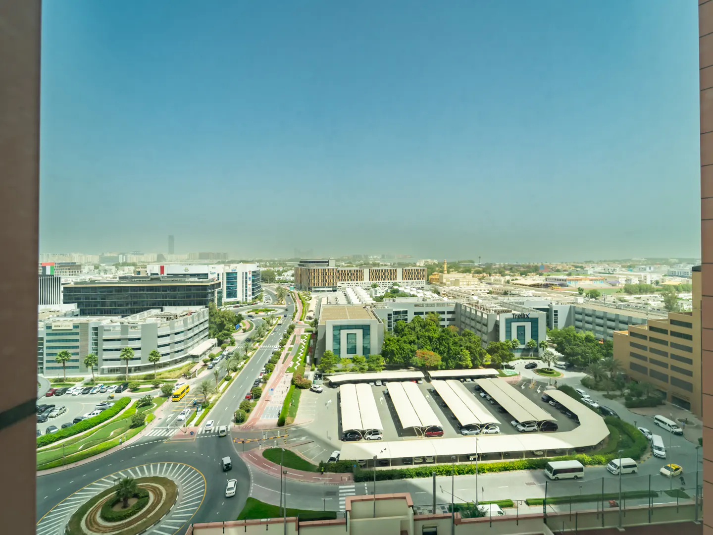 High-angle view of a sunny urban business district with modern office buildings, a roundabout, and shaded parking lots.