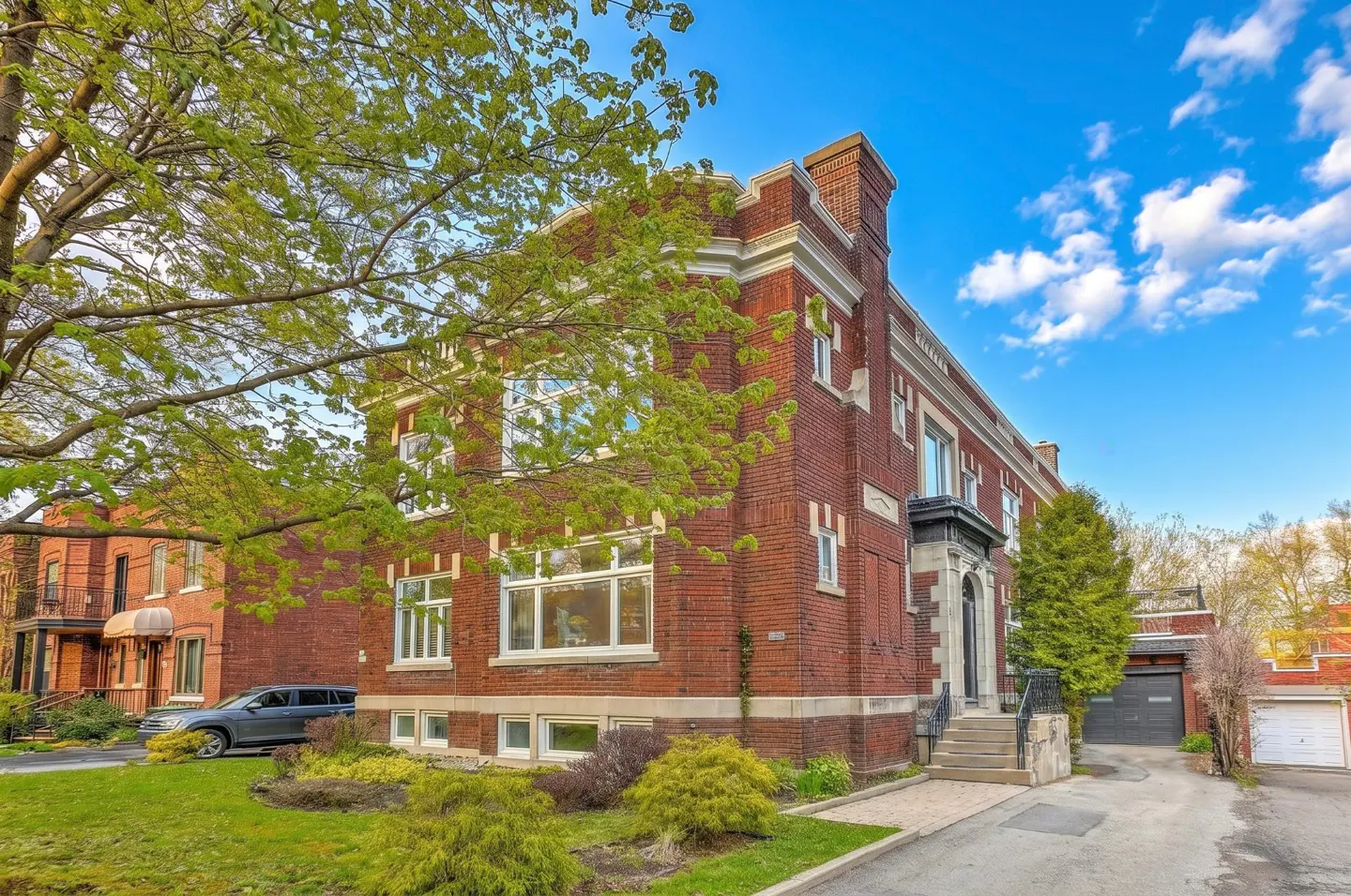 Exterior view of a red brick two-story house with white trim, green trees, and a blue sky.