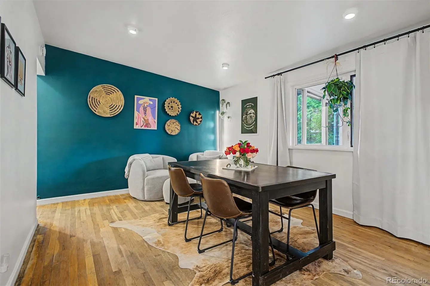 Dining room with a dark teal accent wall, wooden table, brown leather chairs, and a cowhide rug on hardwood floors.