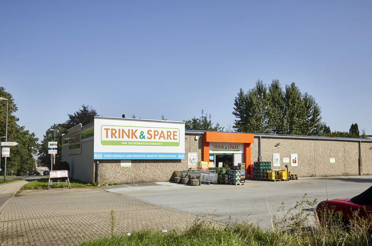 Exterior of Trink & Spare store with orange entrance, large sign, and stacked drinks.