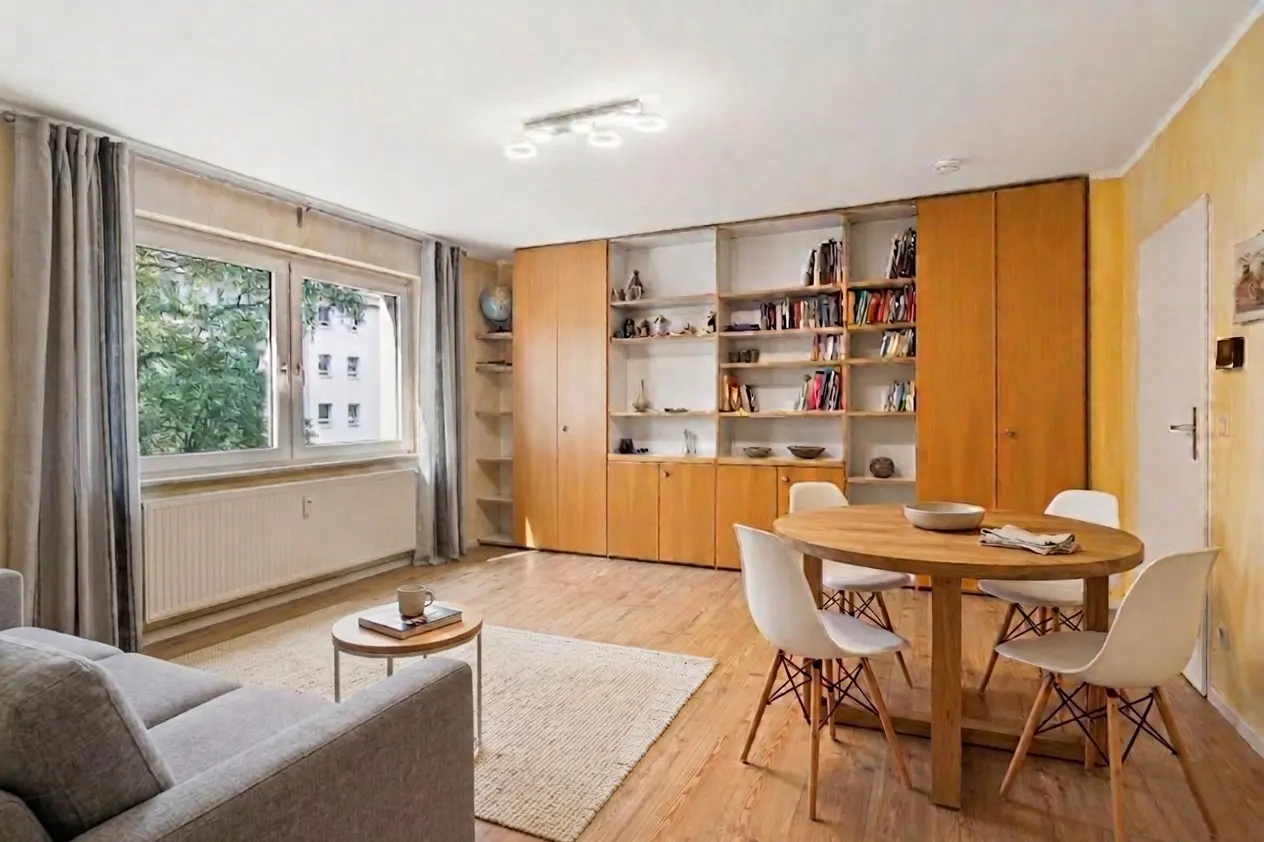 Living room with wood floors, a gray sofa, a round wood table with four white chairs, and a large built-in bookcase.