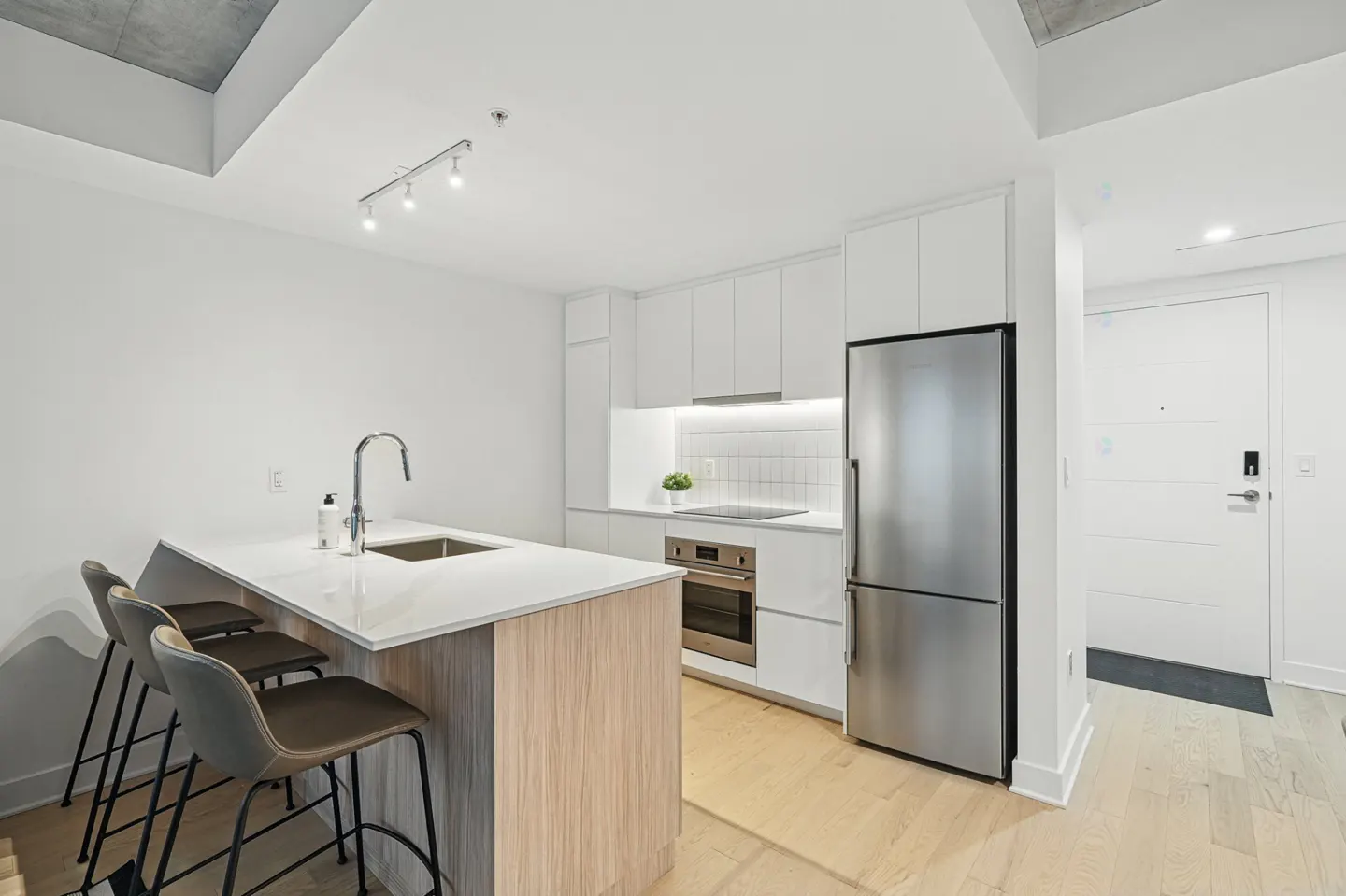 Bright, modern kitchen with white cabinets, stainless steel appliances, and a wood-paneled island with three stools.