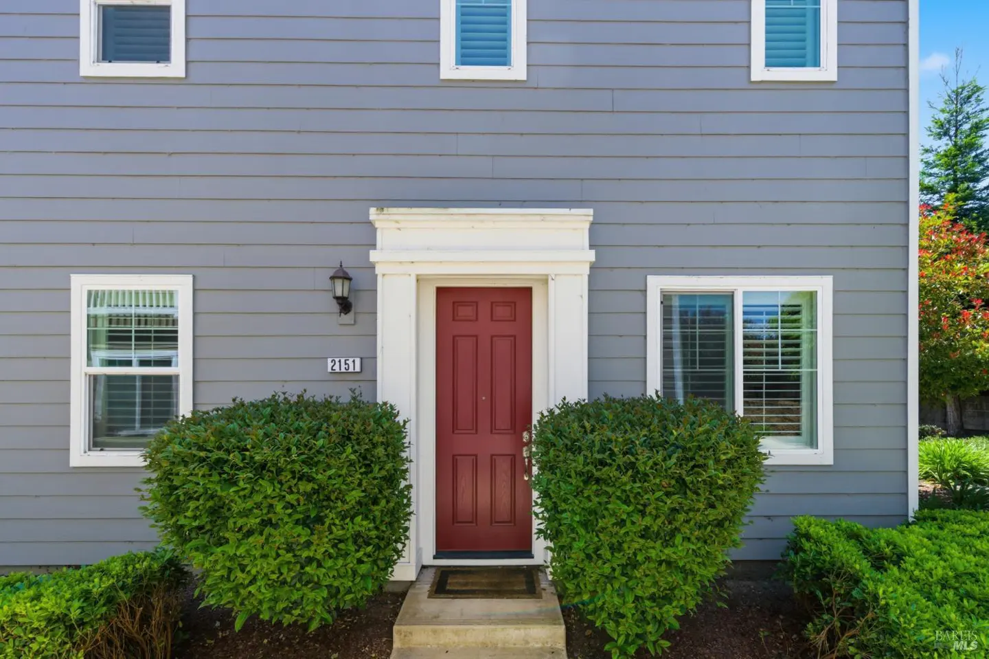 Gray house with a red front door, white trim, and green bushes. The house number "2151" is visible.