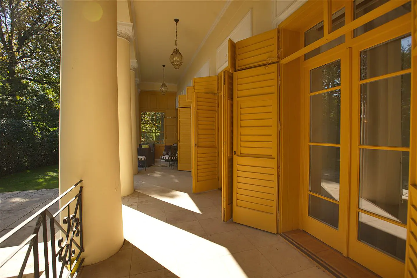 Covered porch with yellow doors and shutters, cream-colored columns, and hanging lanterns.