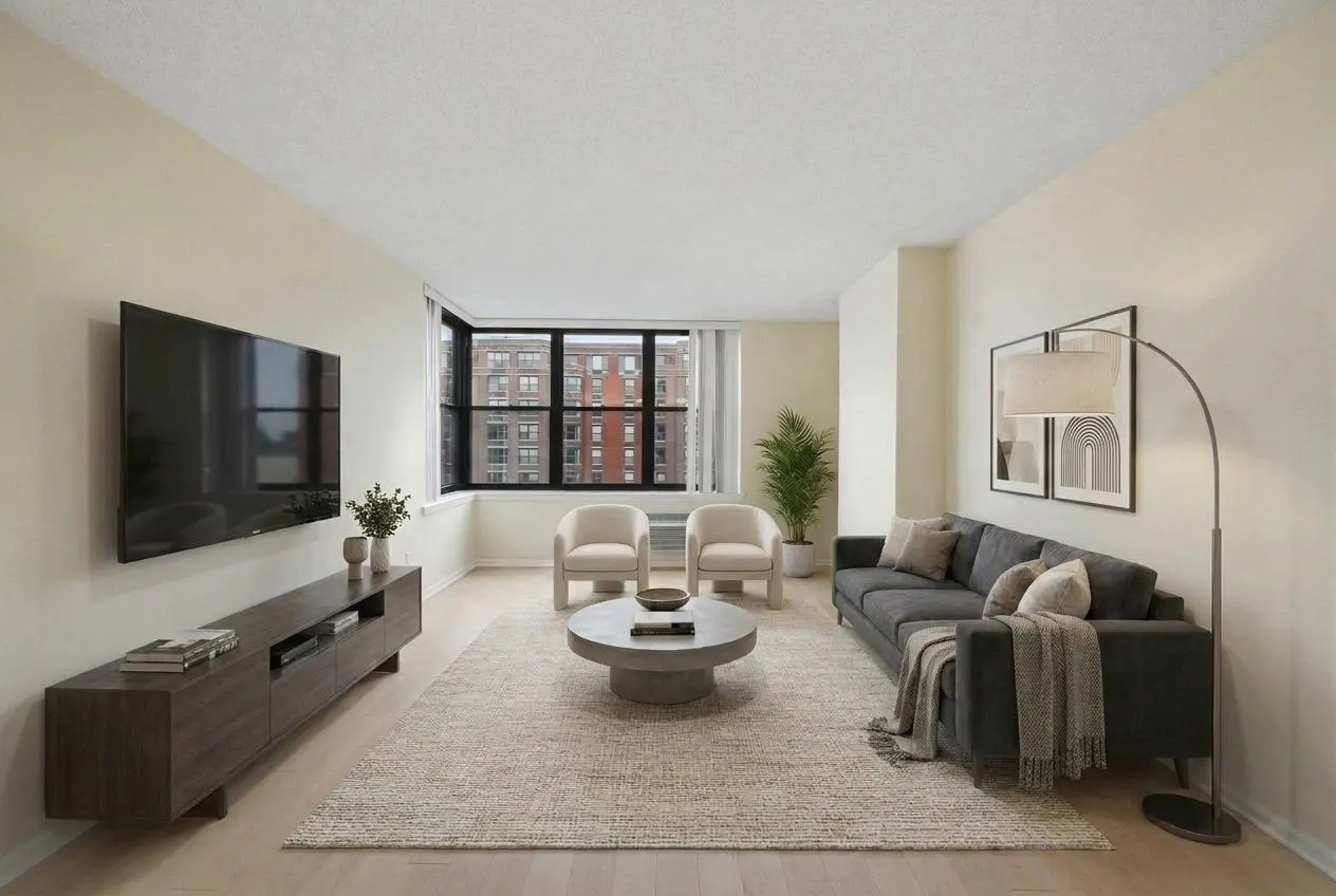 Modern living room with a dark grey sofa, two cream armchairs, a round coffee table, and a wall-mounted TV on a wood console.