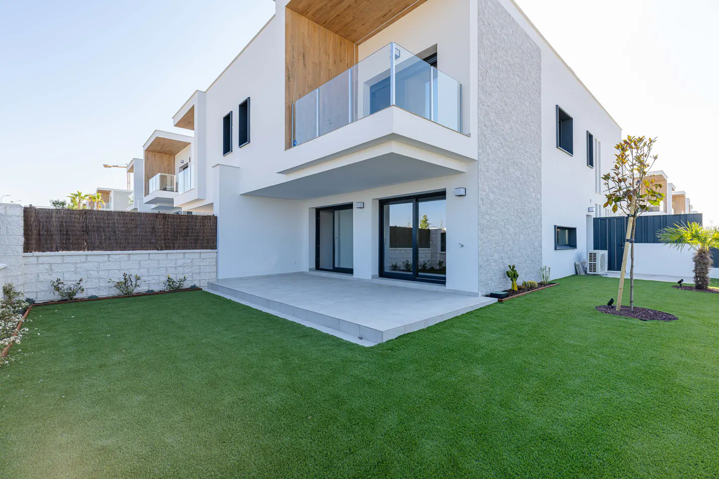 Exterior view of a modern two-story white house with a balcony, patio, and green lawn.