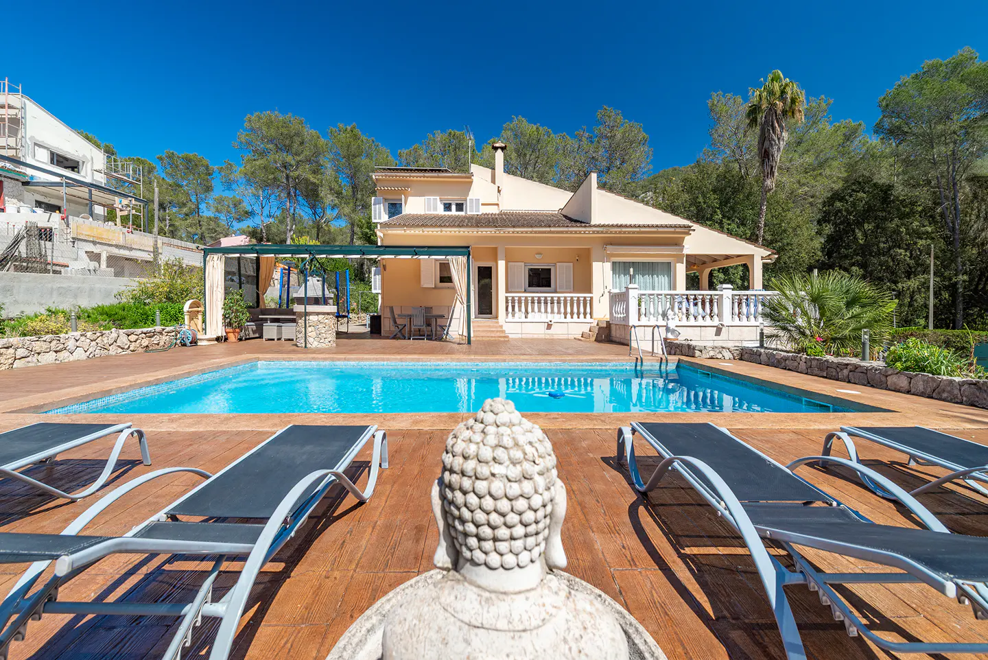 A tan house with a pool, lounge chairs, and a Buddha statue in the foreground.